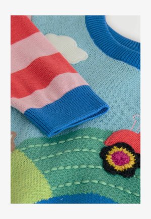 Maglione lavorato a maglia con corpo blu, maniche a strisce rosse e rosa, e dettagli ricamati di un trattore e fiori su un design di paesaggio verde.