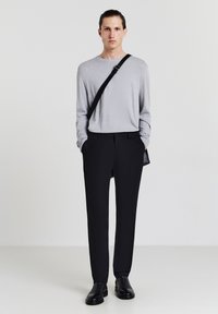 Camicetta grigia a maniche lunghe, pantaloni neri su misura, scarpe nere e una borsa a tracolla. Vestibilità slim, trama liscia, design minimale e colori neutri.