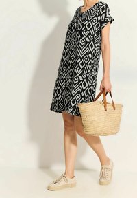 Svart och vit mönstrad klänning med korta ärmar, vävd halmstorpås som har läderhandtag, och beige snörskor.