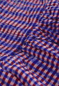 Gros plan sur un tissu froissé avec un motif à carreaux rouge, bleu et beige et une texture tissée visible.