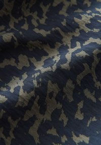 Tessuto con uno sfondo blu scuro e un sottile motivo astratto in beige chiaro, che mette in evidenza una texture liscia e una piega morbida.