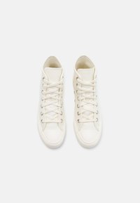 Zapatillas altas de lona color blanco roto con cierre de cordones, ojales metálicos y puntera de goma, que presentan una superficie texturada y un diseño aerodinámico.