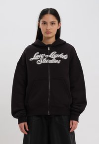 Sweatshirt preto com fecho, apresentando um bolso frontal, ajuste oversized e logótipo bordado em branco "Low Lights Studios" no peito.
