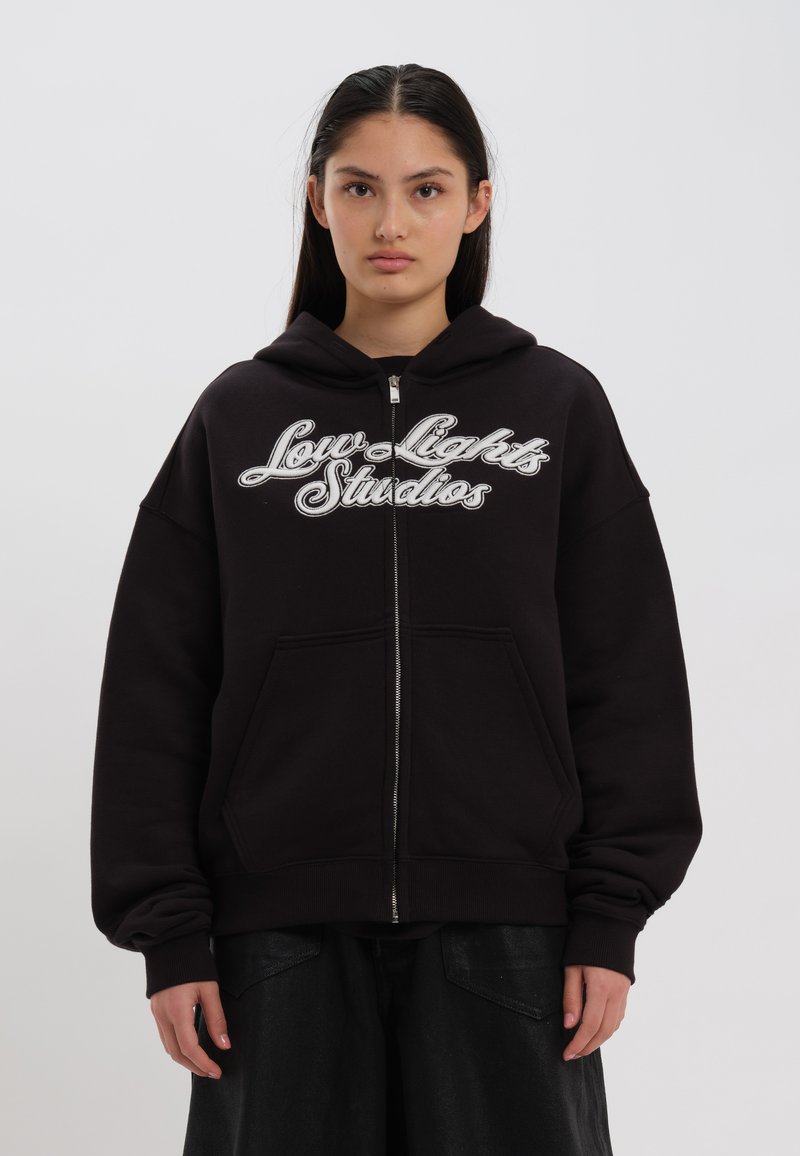 Sweatshirt preto com fecho, apresentando um bolso frontal, ajuste oversized e logótipo bordado em branco "Low Lights Studios" no peito.