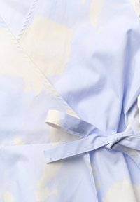 Vaaleansininen kietaisumekko, jossa on valkoisia pilvimäisiä kuvioita, varustettuna solmittavalla vyötäröyksityiskohdalla ja sileällä kankaan tekstuurilla.