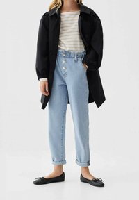 Chaqueta ligera negra con mangas abullonadas sobre una camisa de rayas blanca y beige. Jeans de tiro alto en azul claro y bailarinas negras.