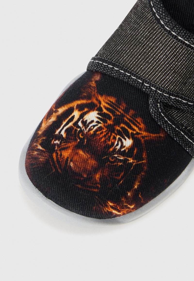 Schwarze Leinenschuhe mit einem lebhaften Tigermuster auf der Zehenpartie, grauer Gummisohle und einem strukturierten Stoffriemen zum Verschließen.