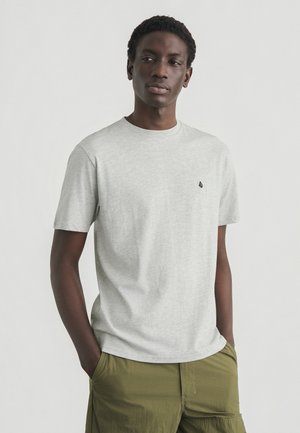 T-shirt gris à manches courtes avec un col rond et un petit emblème noir sur le côté gauche de la poitrine. Tissu doux et léger avec une texture lisse.