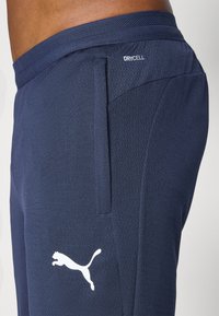 Pantalons de sport navy en tissu texturé avec une taille respirante, comportant des poches latérales et un logo Puma blanc sur la jambe.