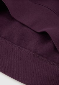 Lila sweatshirttyg som visar en mjuk inre textur, ribbat avslut och slät yta med ett något upphöjt mönster vid kragen.