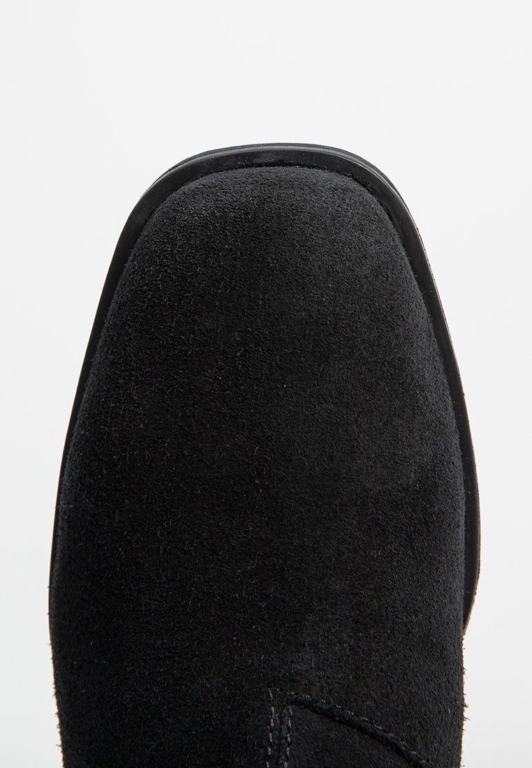 Schwarze Wildleder-Stiefelette mit runder Zehenpartie und glattem, flachem Absatz. Weiche Textur mit minimalen Nähdetails entlang der Seite.