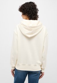 Crème-kleurige hoodie met een ontspannen pasvorm, geribde manchetten en tailleband. Zacht stoffen textuur, weergegeven vanaf de achterkant.