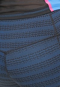 Černé sportovní legíny s modrým tečkovaným vzorem. Materiál vypadá jako elastický s texturovaným povrchem a vyztuženými švy.