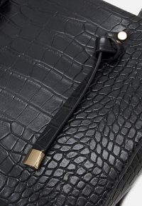 Zwarte leren tas met een gestructureerd krokodillenpatroon, een slanke zwarte schouderband en een gouden metalen accent bij de sluiting.