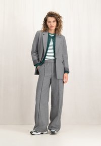Grijs wollen mix pak met wijduitlopende broek en een getailleerde blazer, gelaagd over een groen gestreept sweater. Sneakers maken de look af.