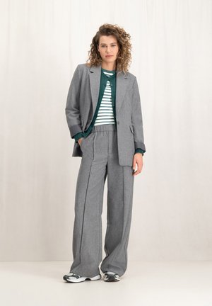 Grijs wollen mix pak met wijduitlopende broek en een getailleerde blazer, gelaagd over een groen gestreept sweater. Sneakers maken de look af.