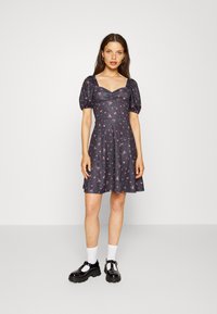 Vestido cinza escuro com mangas curtas e volumosas, corpete franzido e padrão floral rosa. Saia em linha A, até ao joelho, combinado com sapatos pretos robustos.