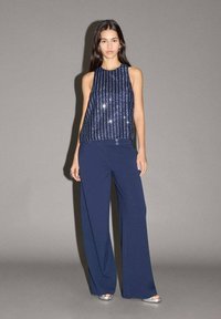 Mornarsko modra brezrokavnica s sequini in vertikalnimi črtami, v kombinaciji s širokimi mornarsko modrimi hlačami in srebrnimi čevlji. Preprost dizajn in gladke teksture.