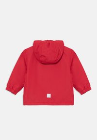 Rote wasserdichte Jacke mit Kapuze, elastischen Bündchen und einem kleinen quadratischen Etikett auf der Rückseite. Glatte Textur und lockere Passform.