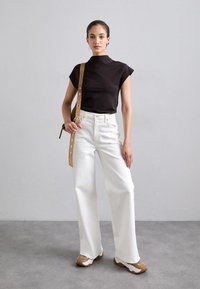Black short-sleeve top, high neck, white wide-leg jeans, tan belt with silver hardware, and beige shoes with a textured sole.