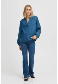 Top in denim con colletto alla mandarino e maniche lunghe, abbinato a jeans in denim a trombetta. Entrambi sono di un blu medio uniforme.