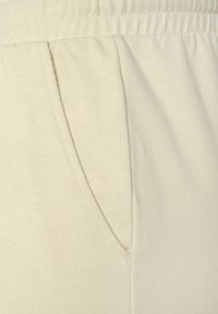  Lichtbeige joggerbroeken met een zachte stoffen textuur, een elastische tailleband en zijzakken met nette stikseldetails.