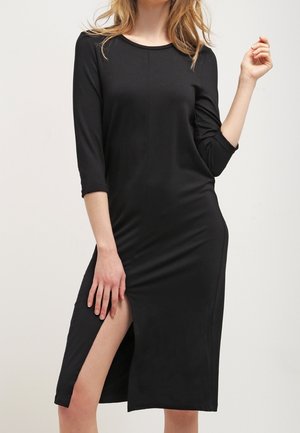 Robe noire à manches longues avec un décolleté rond et une fente sur le côté. Fabriquée à partir d'un tissu lisse et extensible qui épouse les formes du corps.