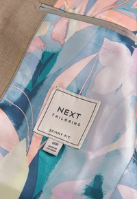Innenausstattung eines maßgeschneiderten Jackets aus leichtem Stoff mit floralem Muster in Pastellblau, Pink und Grün. Etikett mit der Aufschrift "NEXT TAILORING", Größe 40R.