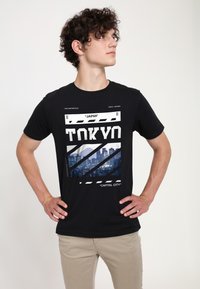 Svart t-shirt med ett grafiskt tryck av Tokyos skyline i modern typografi. Tillverkad av bomull, korta ärmar och rundad hals.