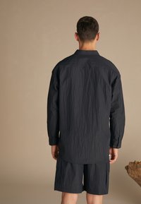 Dark blue, crinkled fabric shirt with long sleeves, buttoned cuffs, pointed collar, and a curved hem, paired with matching shorts.