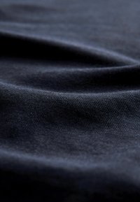 Temno modra tkanina z gladko, rahlo teksturirano površino, ki vključuje mehke gube in subtilen sijaj, poudarjajoč globino in gibanje.