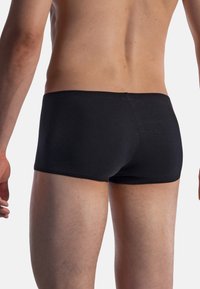 Black cotton boxer briefs with a snug fit. Smooth texture, elastic waistband, and minimalist design. Rear view showing coverage and contours.