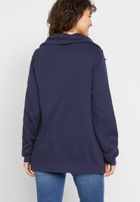 Felpa blu navy con collo a cowl, maniche lunghe, vestibilità rilassata e orlo a costine. Tessuto liscio senza motivi o dettagli visibili.