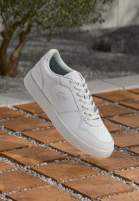 White leather sneaker with a low-top design, smooth texture, lace-up closure, perforated toe, and embossed logo on the side.