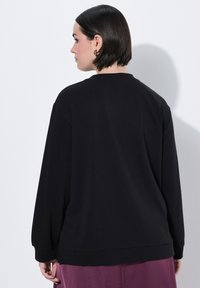 Svart sweatshirt med avslappnad passform, featuring långa ärmar och rundad hals. Slät textur och ribbad mudd vid nederkant.