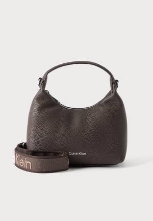 Kleine, dunkelbraune Handtasche aus strukturiertem Leder mit Henkel, Calvin-Klein-Logo und abnehmbarem, gebrandetem Schulterriemen im Vordergrund.
