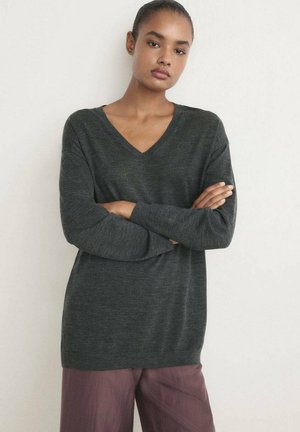 Suéter de punto gris oscuro con escote en V, mangas largas y corte relajado, combinado con pantalones burdeos claros. Tejido texturizado.