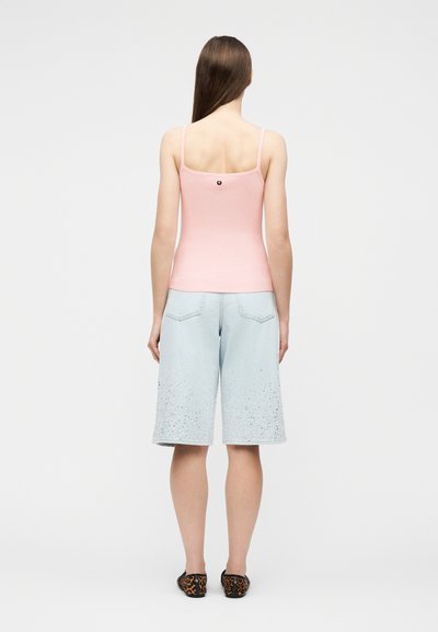 Γυναίκα που στέκεται με την πλάτη, φοράει ανοιχτό ροζ τοπ με λεπτές τιράντες, ανοιχτό γαλάζιο σορτς μήκους μέχρι το γόνατο και πλατφόρμες με λεοπάρ μοτίβο.