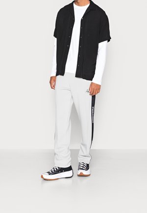 Sort kortærmet skjorte, hvid langærmet skjorte under, grå sweatpants med sorte sidelister og branding, sorte sneakers med hvide detaljer.