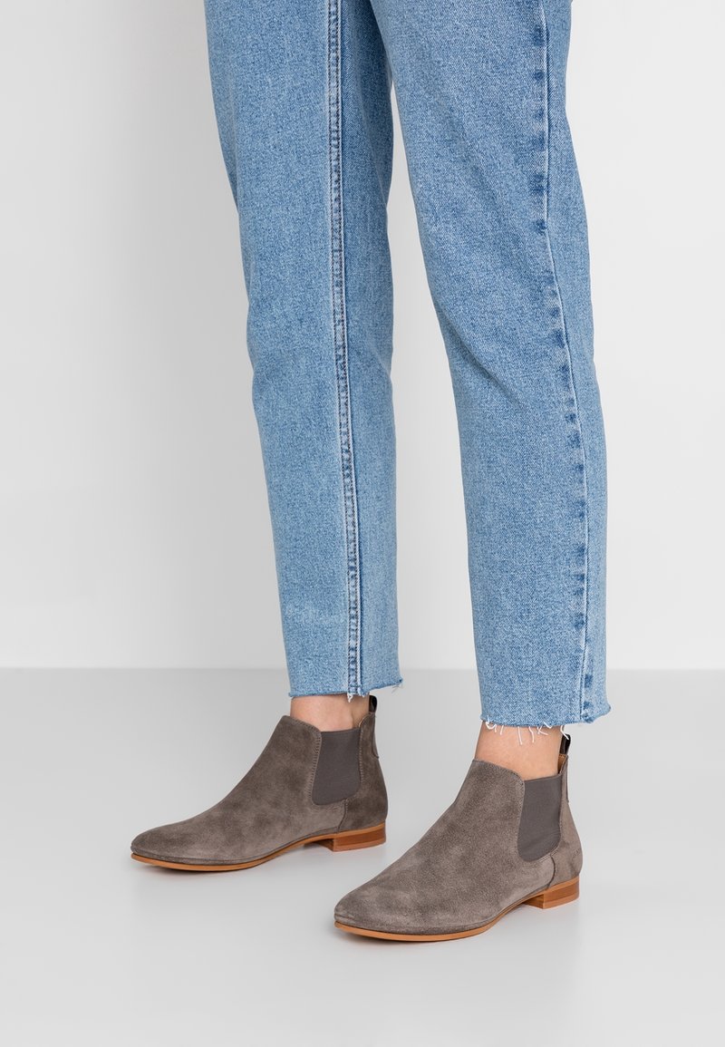 Bottines chelsea en suede gris avec des panneaux élastiques sur les côtés et une semelle en bois marron, associées à un jean en denim bleu cropped.
