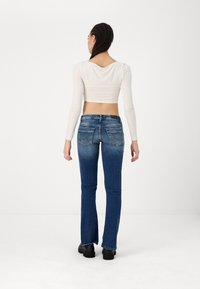 Fitted cream long-sleeve top with scoop back, paired with flared dark blue jeans featuring a faded wash and back pocket stitching details.