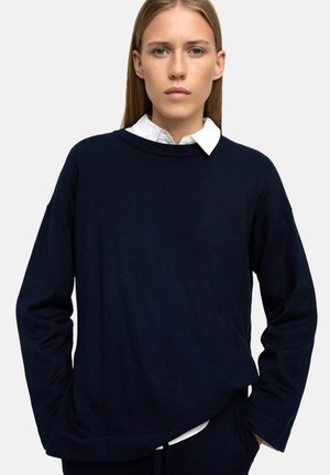 Granatowy sweter wełniany z szerokim dekoltem i długimi rękawami, charakteryzujący się lekko luźnym fasonem oraz warstwą białej koszuli z kołnierzykiem pod spodem.