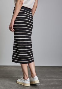 Gonna midi a maglia con strisce orizzontali nere e crema. Vita a coste e silhouette aderente, abbinata a sneakers bianche su una superficie testurizzata.