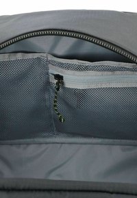 Interno di uno zaino nero con una tasca a rete grigia con zip e tirazip neri, accentuata da dettagli verdi, rivestimento in tessuto grigio liscio.