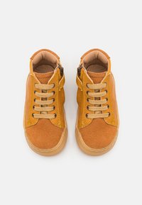 Gulbrune lær-sneakers har en overdel i både ruskinn og glatteslær, runde snører og glidelås på siden. Gummisåle og forsterkede sømdetaljer.