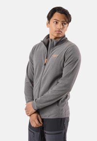 Giacca in pile grigia con collo alto, cerniera arancione e dettaglio del logo. Presenta maniche lunghe e tasche laterali per la funzionalità.