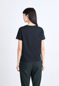 Zwarte katoenen t-shirt met korte mouwen, klassieke ronde hals en een rechte snit, gecombineerd met donker groene broek. Gladde textuur, geen patronen.