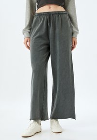 Grijze wijde broek gemaakt van zachte stof, met een elastische tailleband en zijzakken, gecombineerd met witte sneakers.