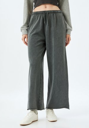 Grijze wijde broek gemaakt van zachte stof, met een elastische tailleband en zijzakken, gecombineerd met witte sneakers.