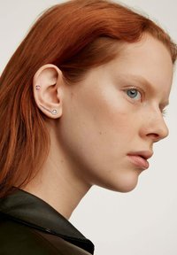 Pendientes de plata exhibidos en la oreja de un modelo; uno tiene un diseño de gema redonda, mientras que el otro presenta una forma lineal con múltiples gemas.